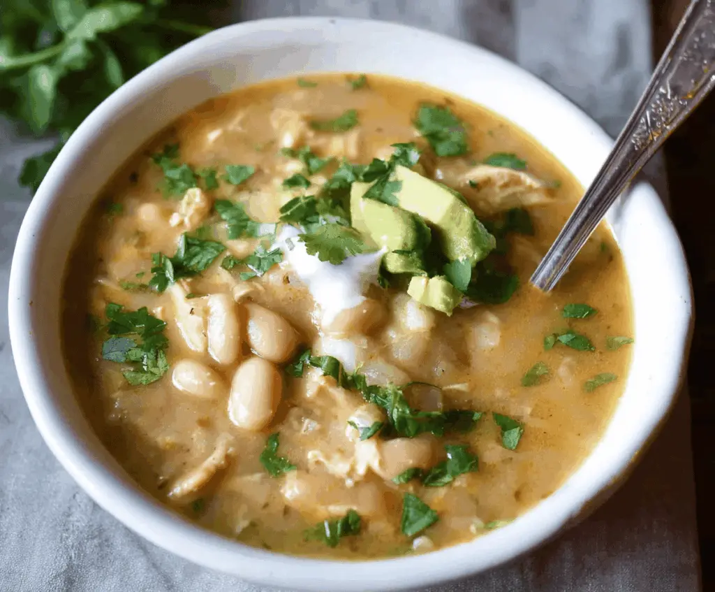 A steaming bowl of Creamy White Bean Enchilada Soup topped with cheese, cilantro, and sour cream, served with tortilla chips on the side.