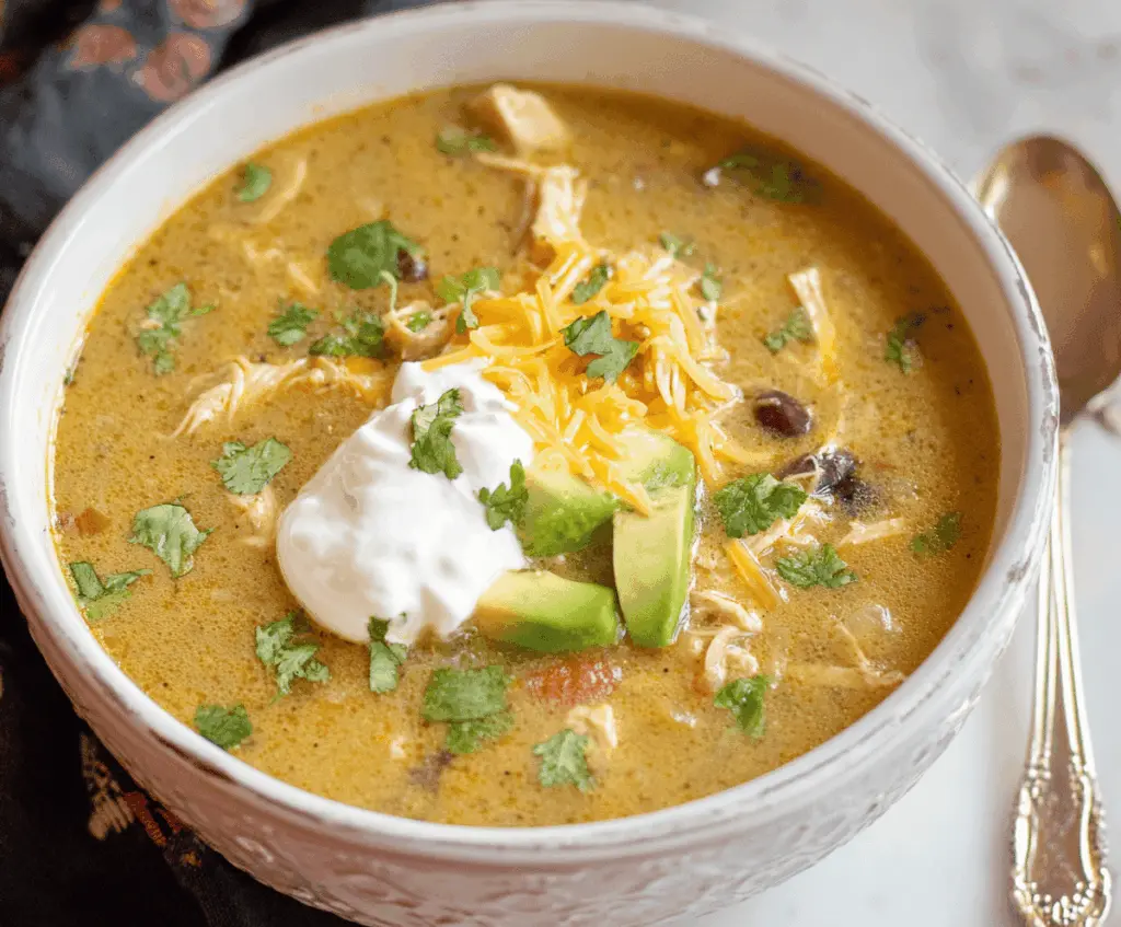 Creamy green enchilada chicken soup topped with shredded cheese and fresh cilantro in a bowl