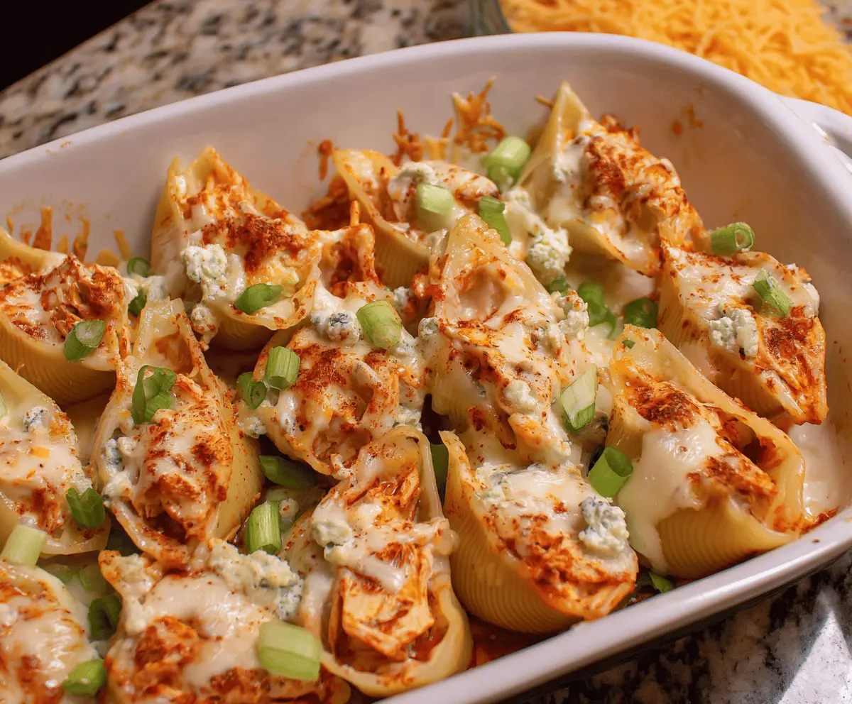 Creamy buffalo chicken stuffed shells topped with melted cheese, garnished with green onions and served with celery sticks for a flavorful appetizer or main dish.