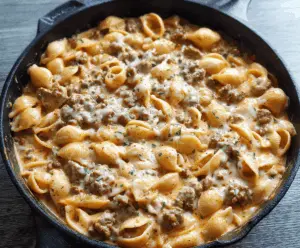 Creamy beef and shell pasta dish topped with melted cheese and fresh herbs, featuring tender ground beef in a rich, savory sauce