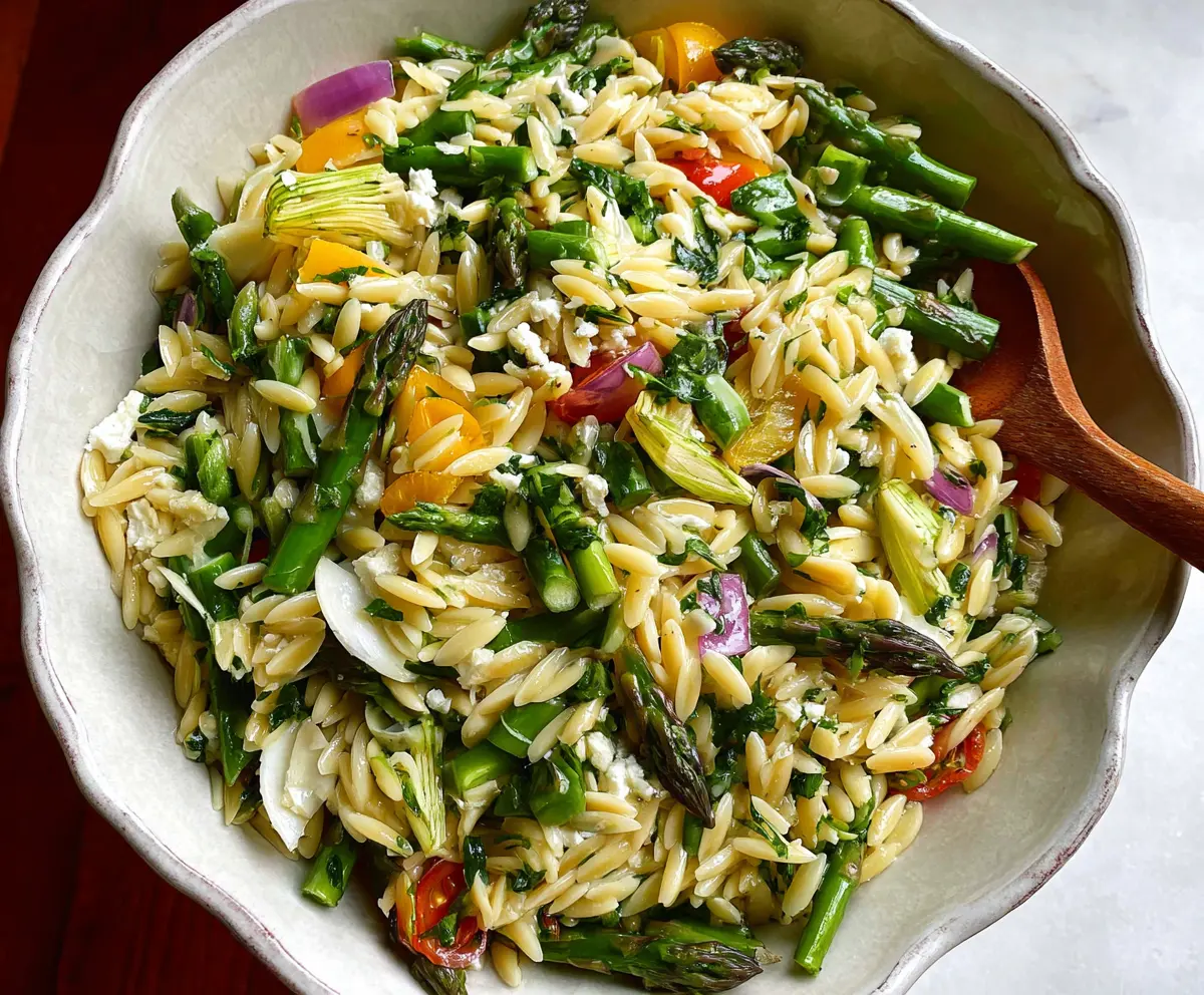Colorful orzo salad with fresh asparagus and herbs in a white bowl for a healthy meal.