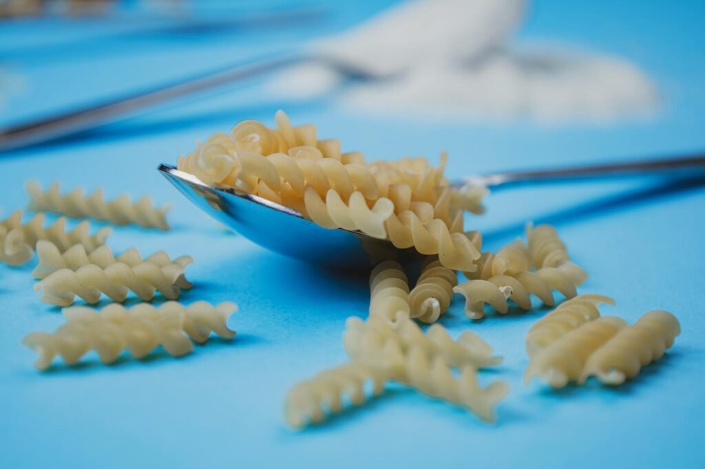 A skillet of pasta sauce with a spoon, lemon wedge, black pepper, and grated cheese on a kitchen counter