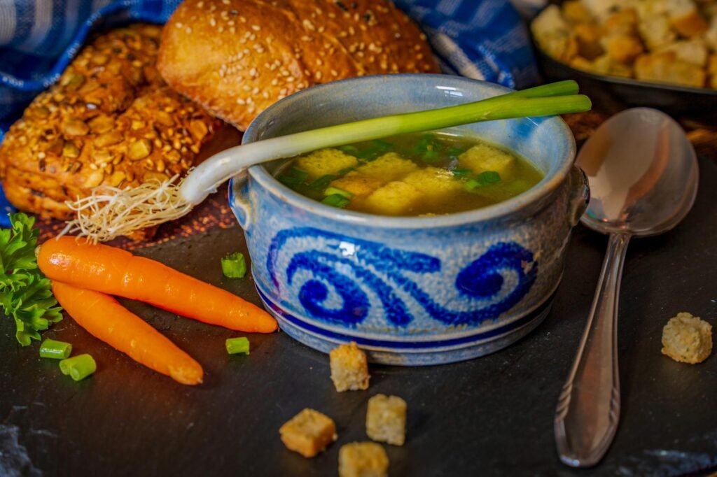 Broth, beans, onions, carrots, and celery arranged on a kitchen counter for soup prep