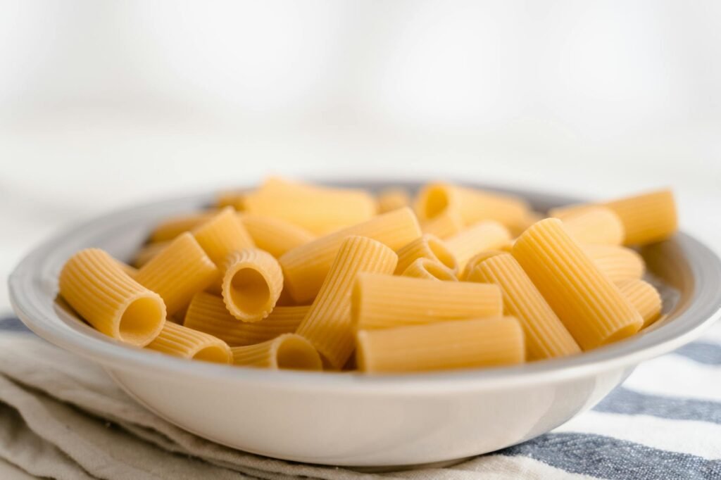 Bowls of different pasta shapes, including ridged and twisted varieties, on a wooden kitchen surface
