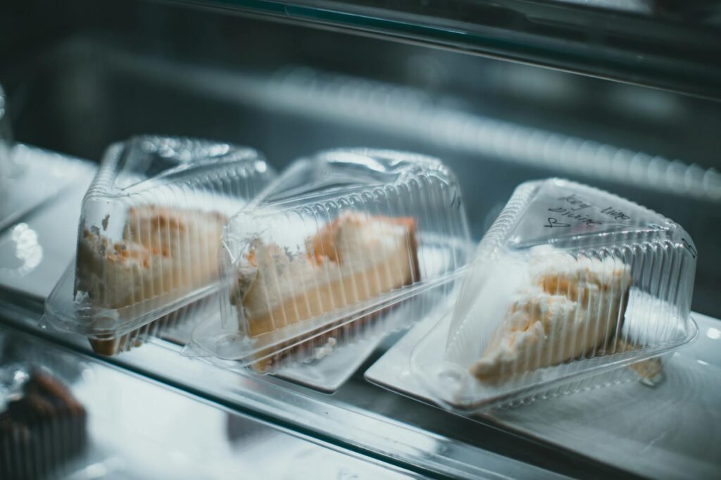 Labeled lunch containers arranged on a refrigerator shelf beside a thermometer